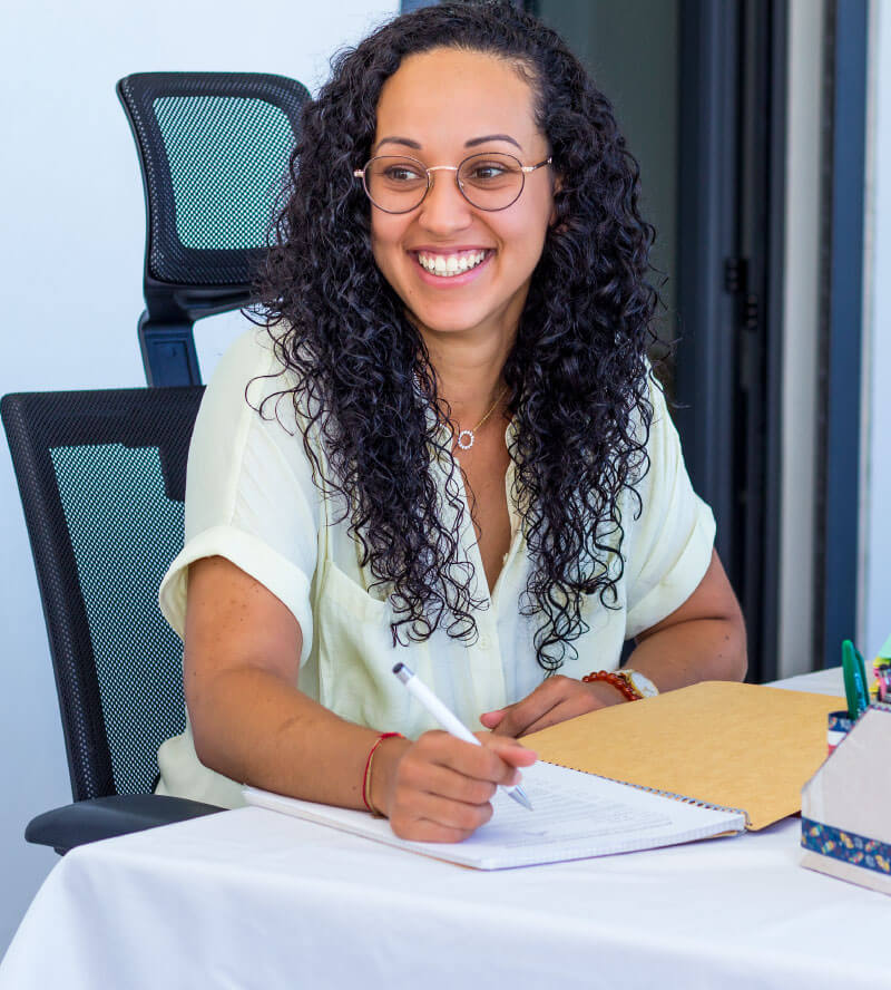 Olivia Morel, responsable marketing à La Réunion, assise à son bureau. Elle rit en écrivant dans un cahier.